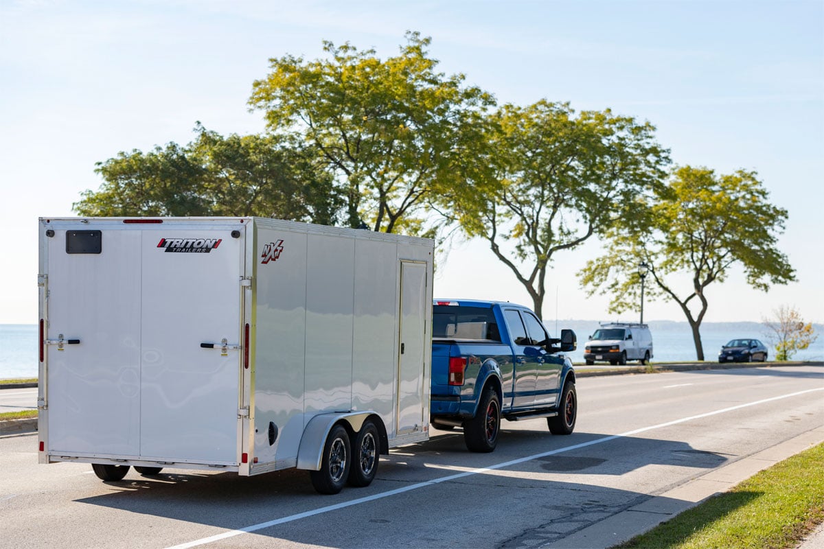 Blue Truck Hauling Triton Enclosed Snow Cargo NXT Series Trailer On Highway